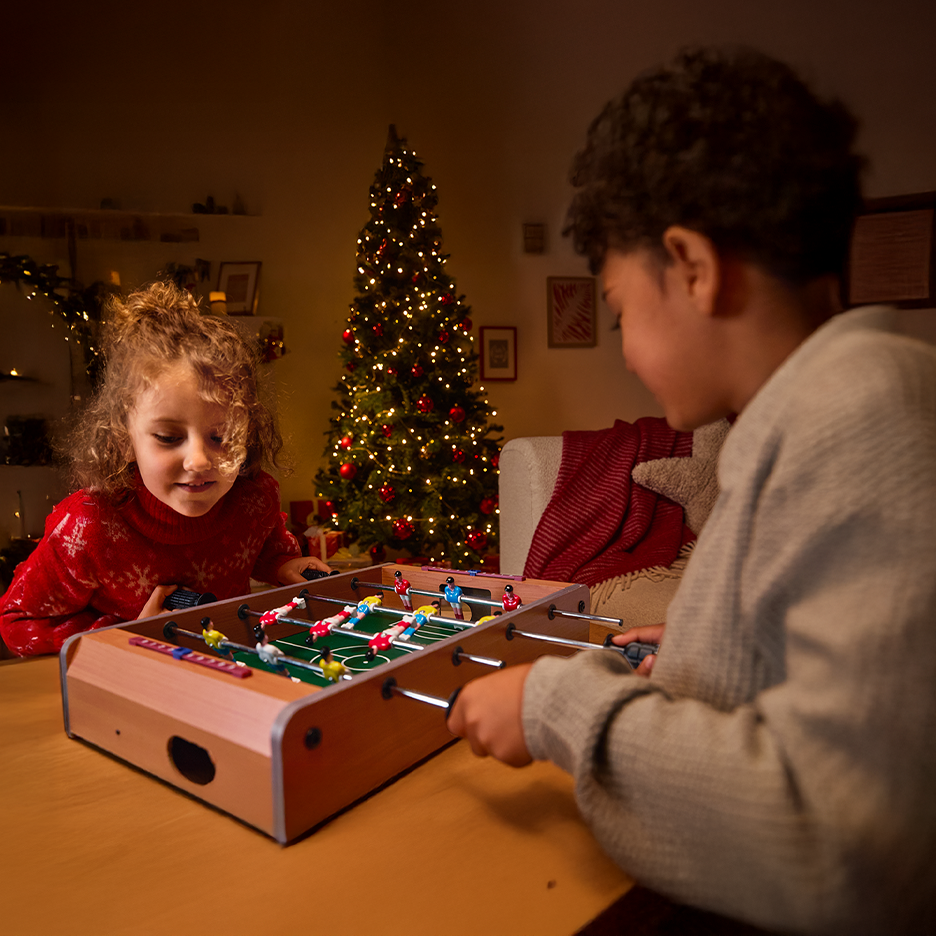 Dwoje dzieci grających w piłkarzyki przy choince.