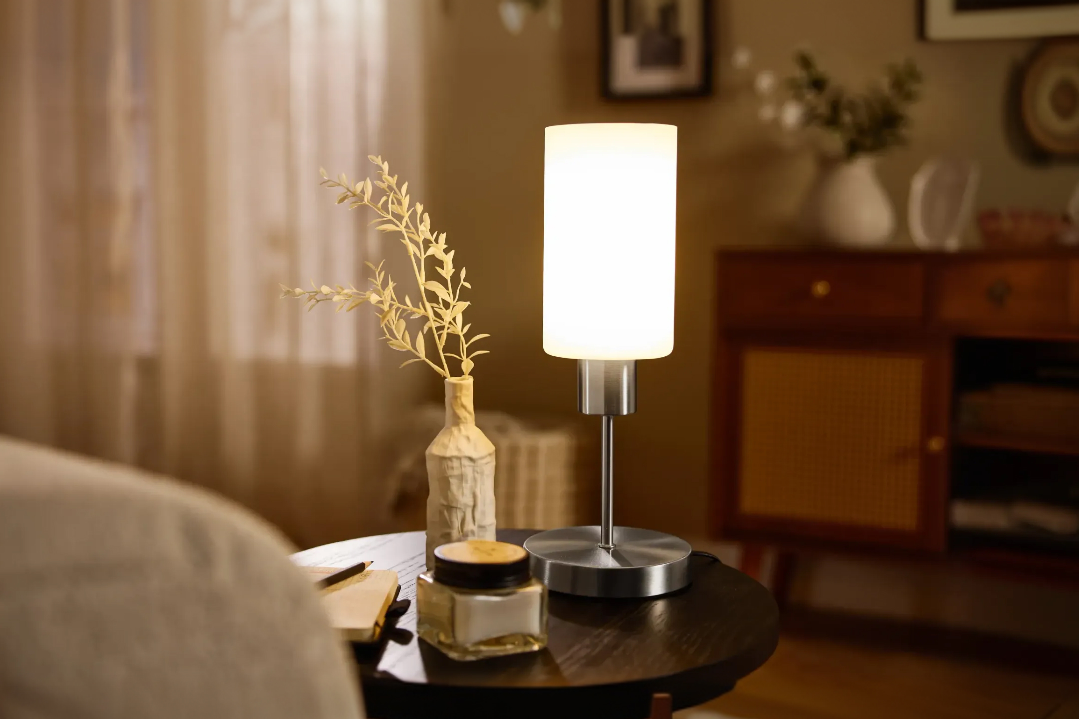 Lampa stołowa na okrągłym stoliku z dekoracją i słoiczkiem w salonie.