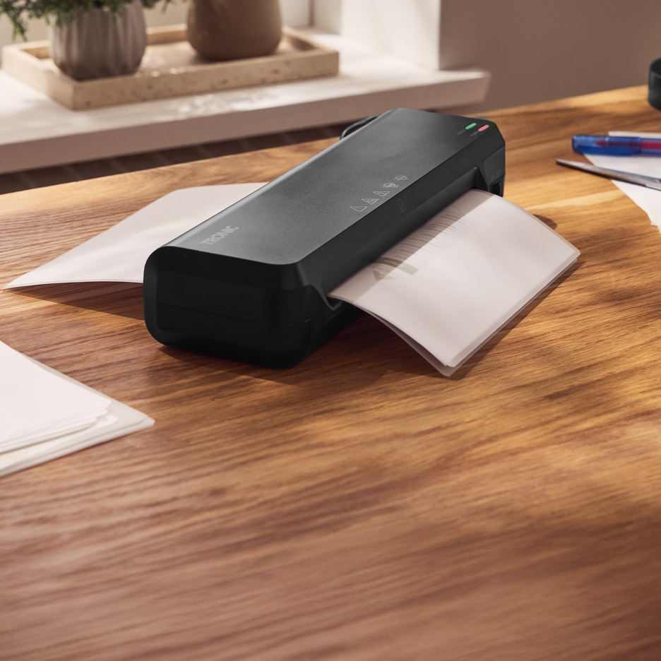 Czarna laminarka TRONIC laminująca dokumenty na drewnianym biurku.