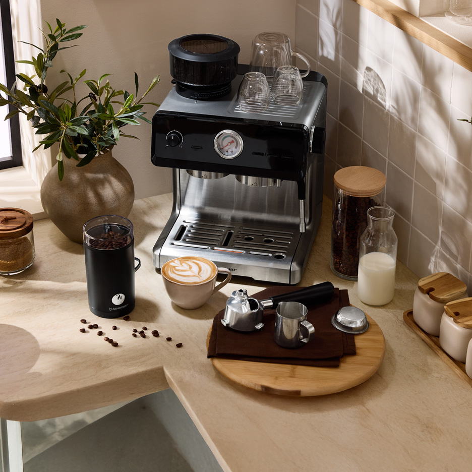 Ekspres do kawy Silvercrest z młynkiem, filiżanką latte i akcesoriami na blacie.