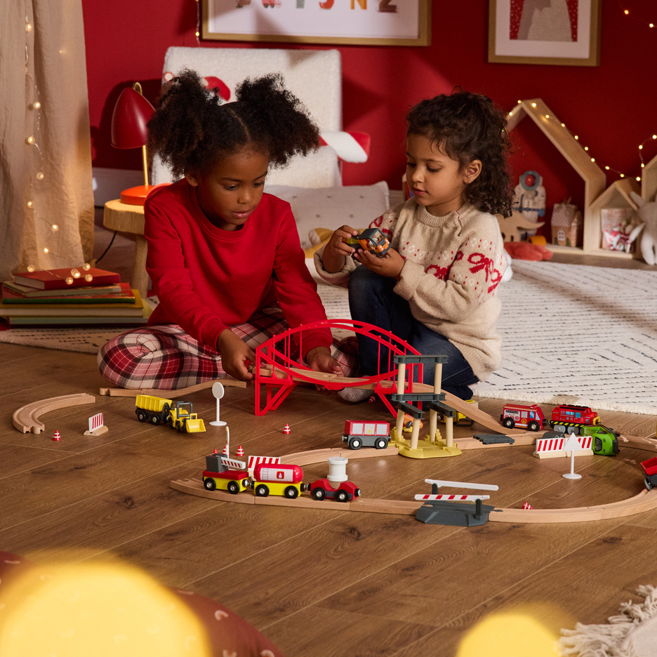 Dwoje dzieci bawi się drewnianą kolejką i mostem w świątecznym pokoju.