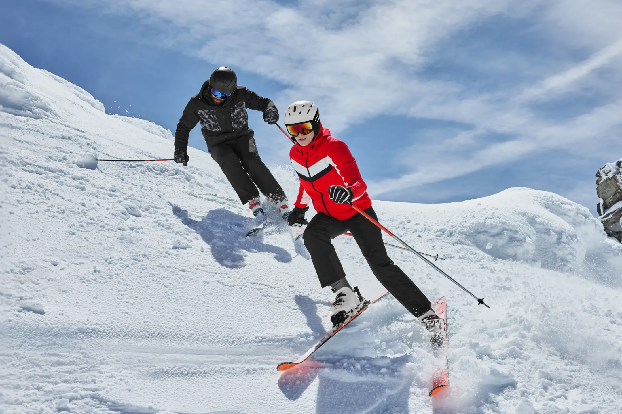 Dwie osoby w kaskach i goglach narciarskich zjeżdżające na nartach po zaśnieżonym stoku.