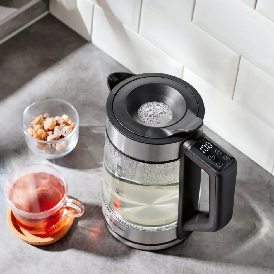 Szklany czajnik Silvercrest z wyświetlaczem, filiżanka herbaty i cukier kandyzowany na blacie.