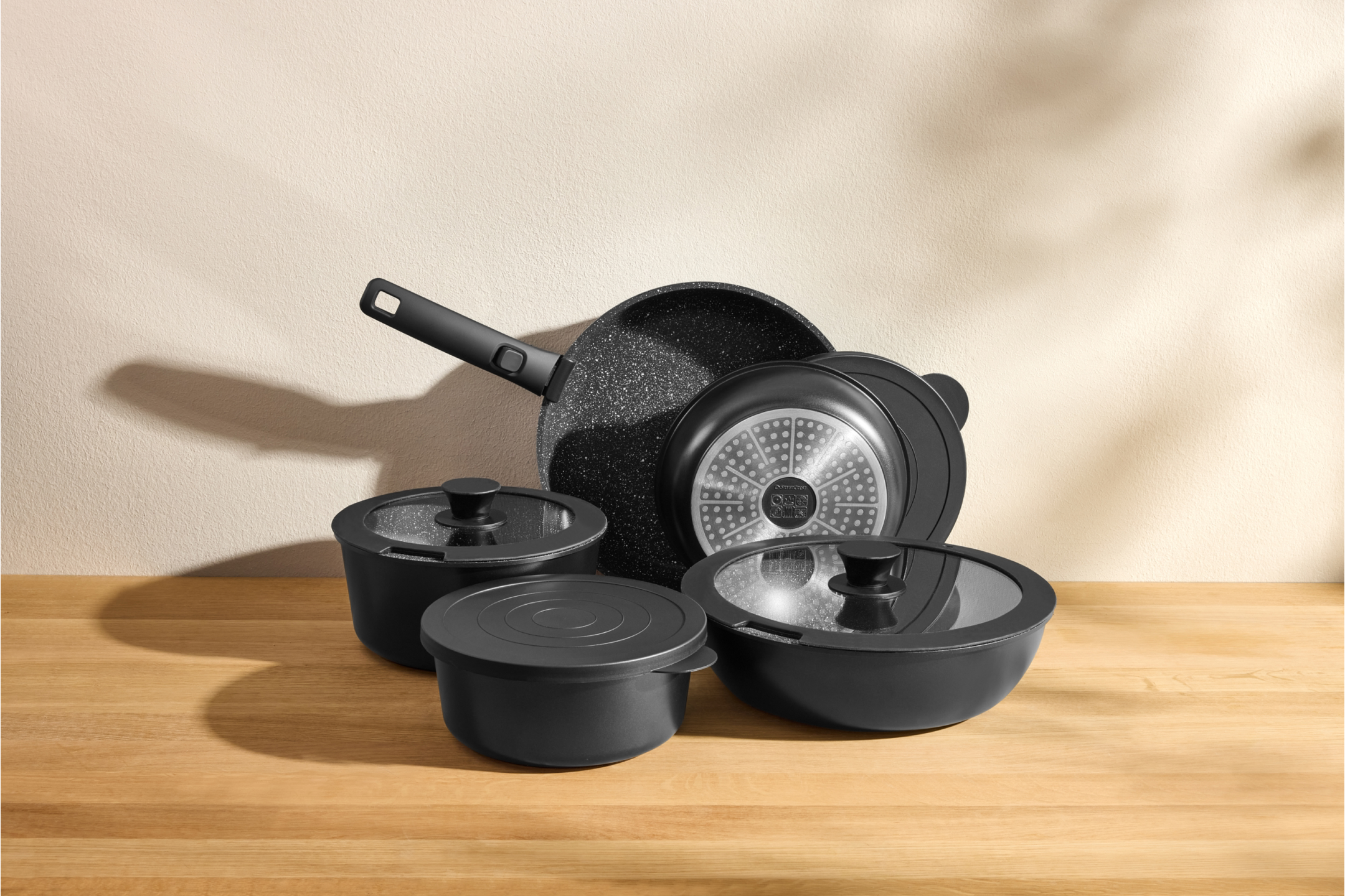 Zestaw czarnych patelni i garnków z pokrywkami na drewnianym blacie.