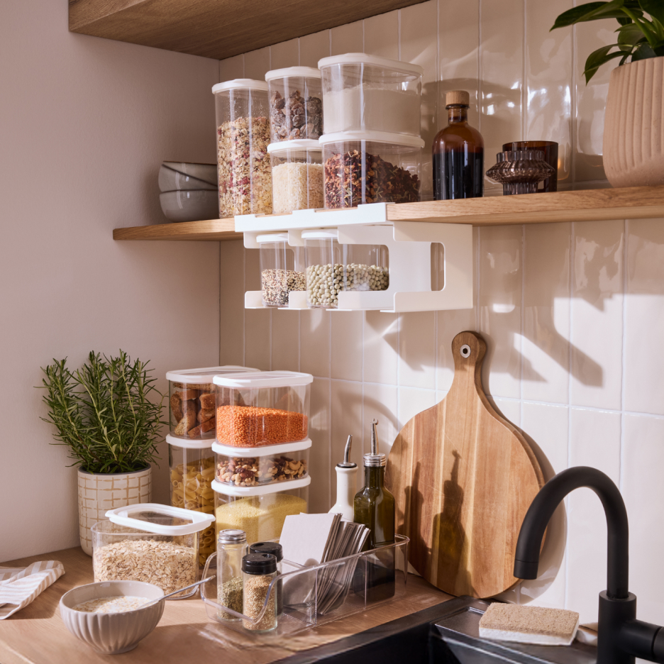 Przechowywanie żywności w kuchni: przezroczyste pojemniki na półkach i podwieszane, przyprawy, deska do krojenia.