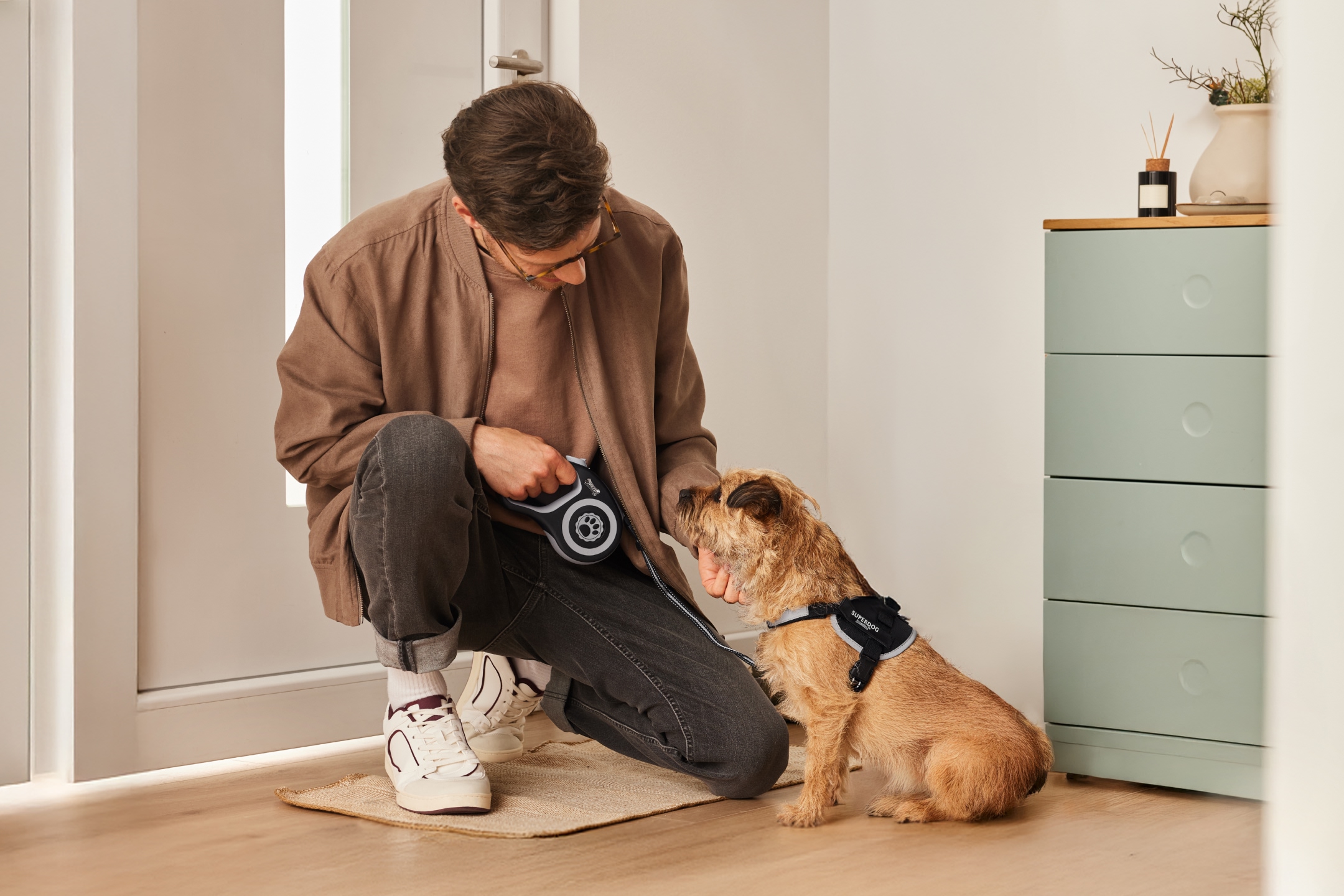 Mężczyzna z psem w szelkach Superdog i smyczą Flexi, przygotowujący się do spaceru.