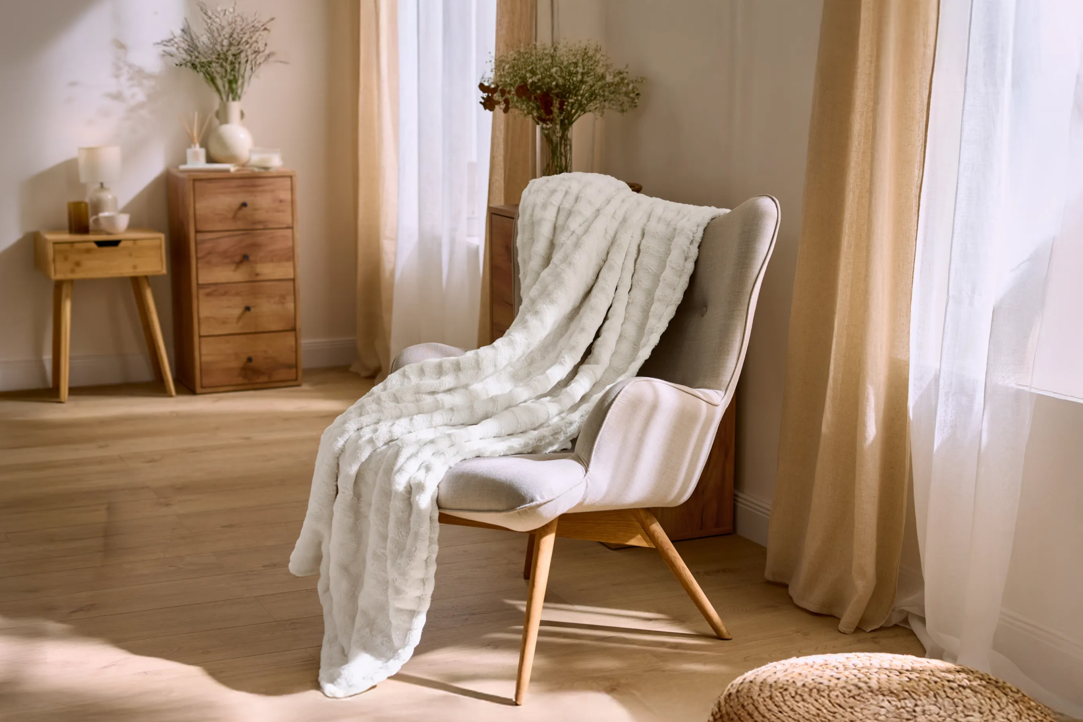 Przytulny salon z jasnoszarym fotelem, białym puszystym kocem i drewnianymi meblami.