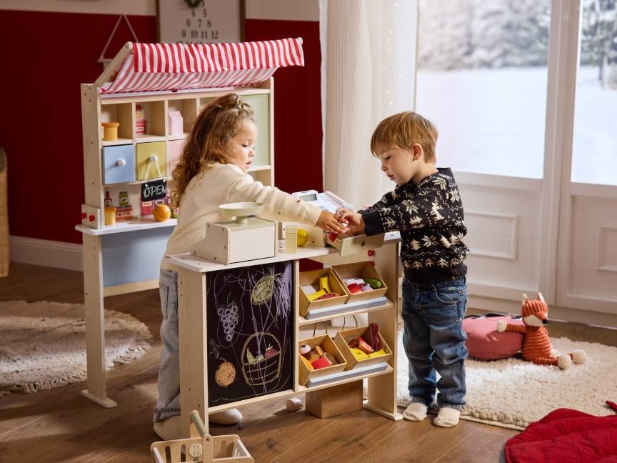 Dzieci bawiące się drewnianym straganem z zabawkami, udając sprzedawców i kupujących.