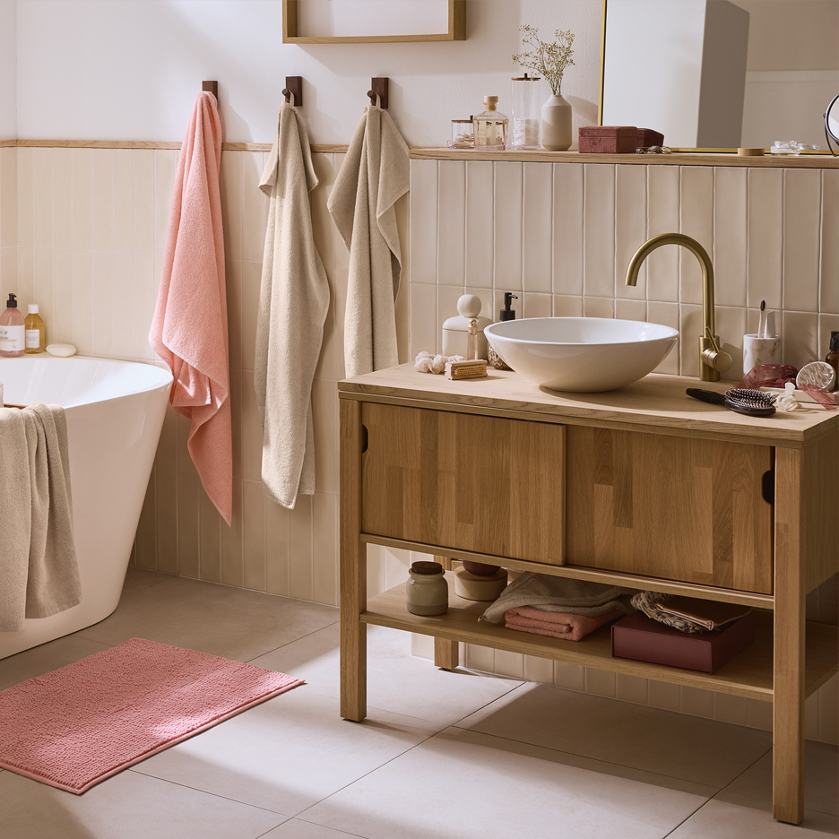 Łazienka z drewnianą szafką pod umywalkę, wanną i różowym dywanikiem.