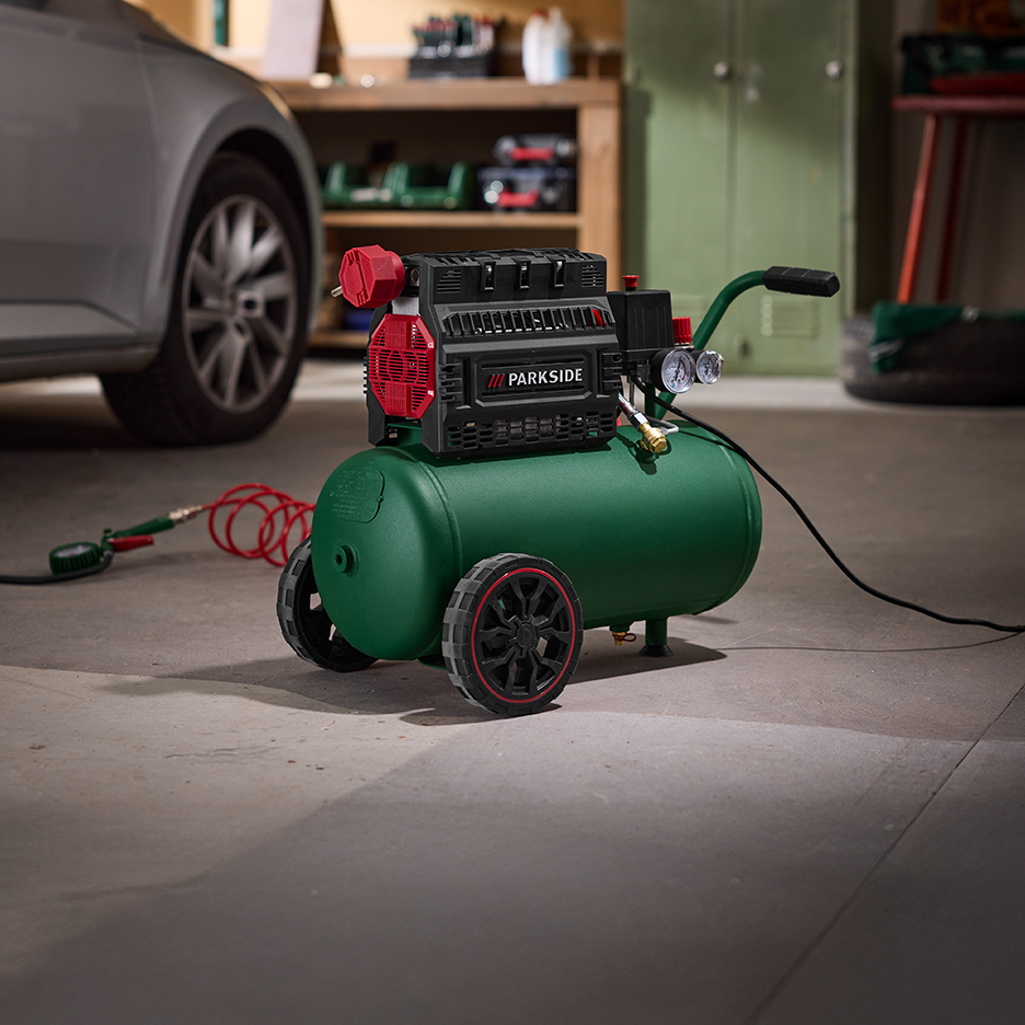 Zielona sprężarka powietrza z manometrami i wężem, obok samochodu w garażu.