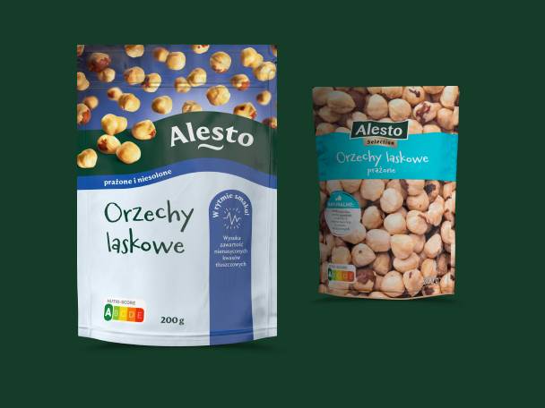 Dwa opakowania orzechów laskowych, prażonych i niesolonych, na ciemnozielonym tle.