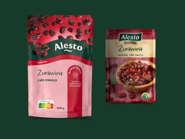 Dwa opakowania suszonej żurawiny, jedno w różowym opakowaniu z napisem „całe owoce”, drugie w beżowym z miską żurawiny.