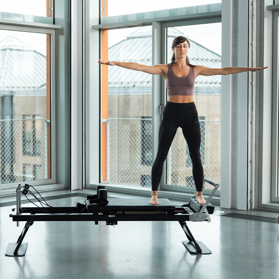 Kobieta ćwicząca Pilates na reformerze, z rozłożonymi ramionami.