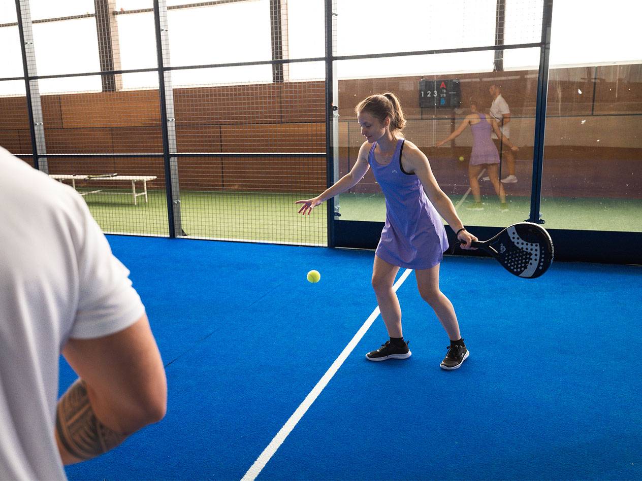 Kobieta w fioletowej sukience sportowej gra w padla z rakietą i piłką.