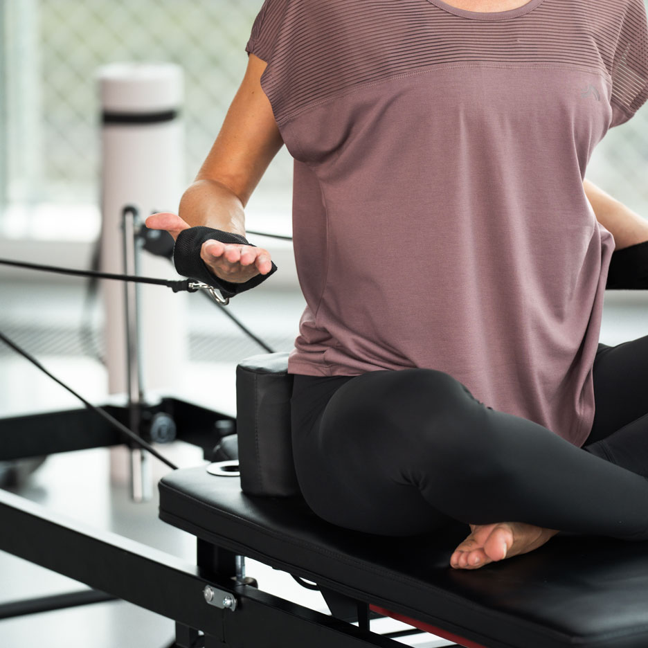 Kobieta ćwicząca Pilates na reformerze, w czarnych legginsach i fioletowym topie.