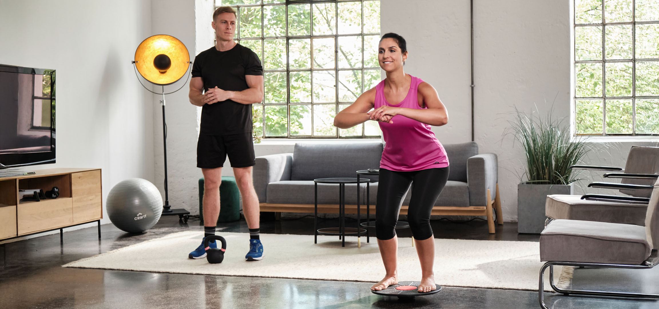 Kobieta i mężczyzna ćwiczą w domu z deską balansową i kettlebell.