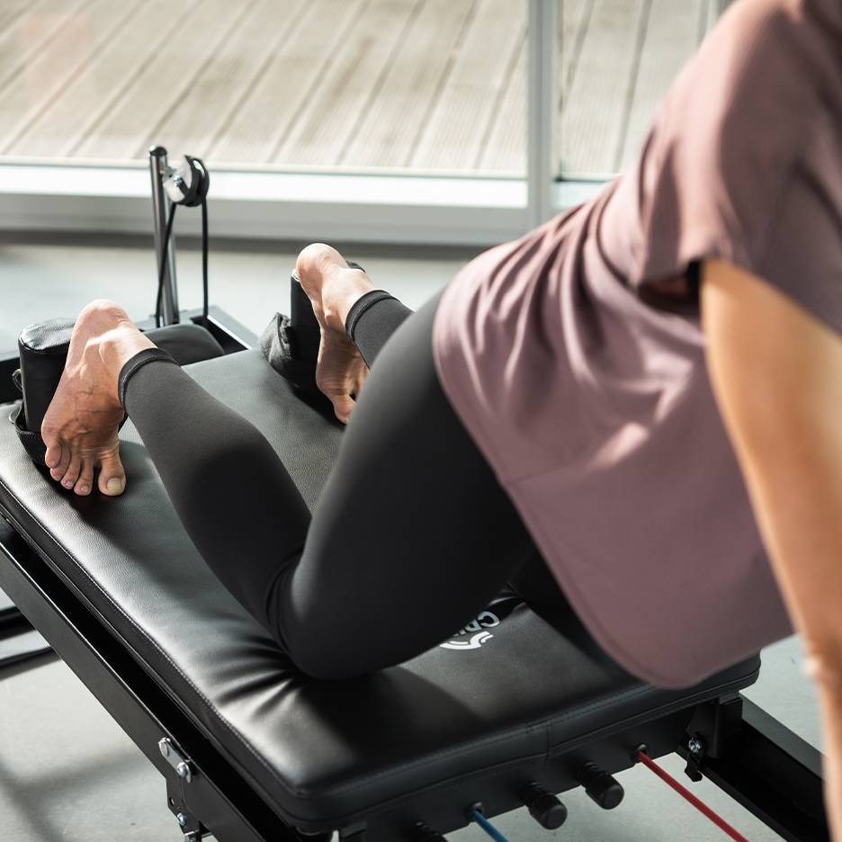 Kobieta ćwicząca na czarnej maszynie do pilatesu ze stopami w paskach.