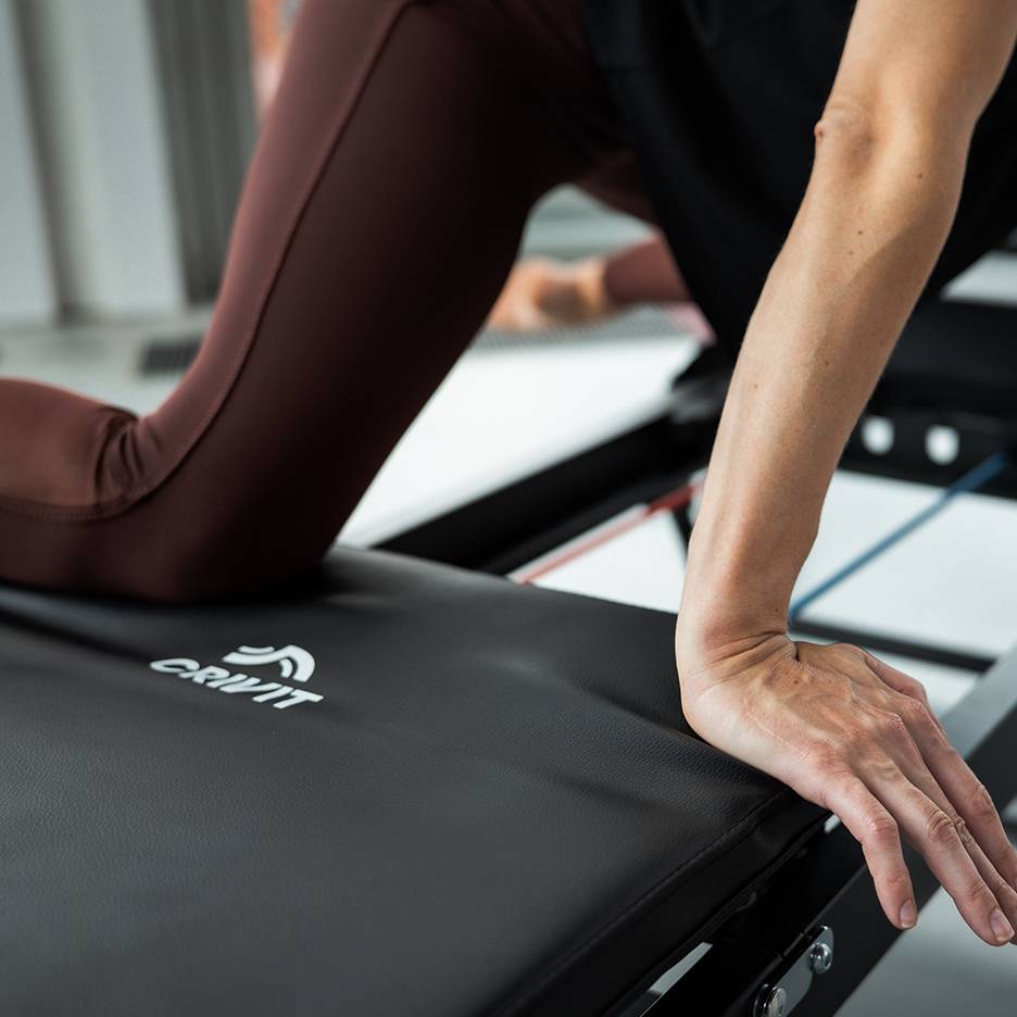 Kobieta ćwicząca na sprzęcie fitness Crivit w brązowych legginsach do jogi.