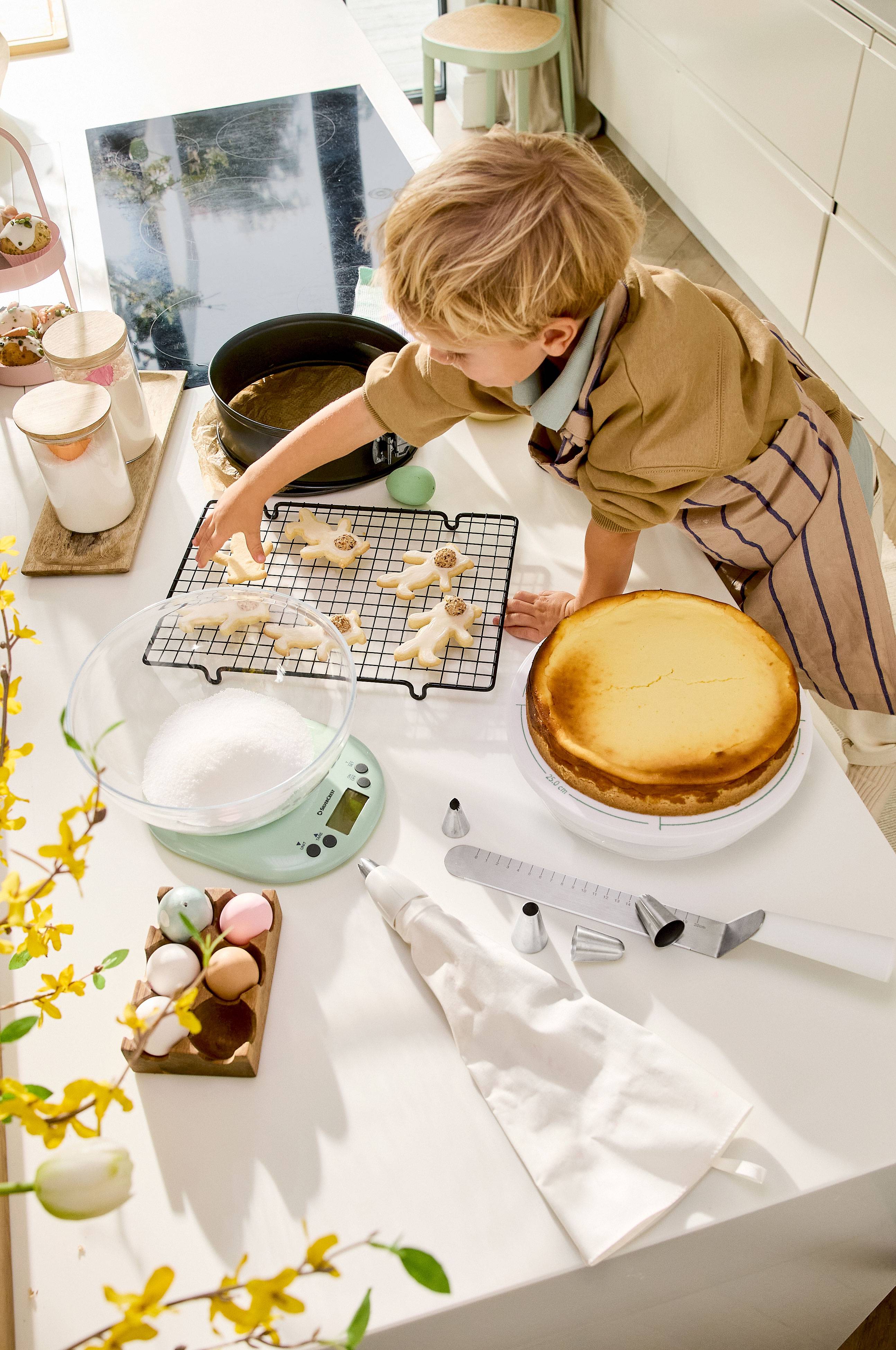 Dziecko dekoruje ciasteczka wielkanocne, z sernikiem i akcesoriami do pieczenia na stole.
