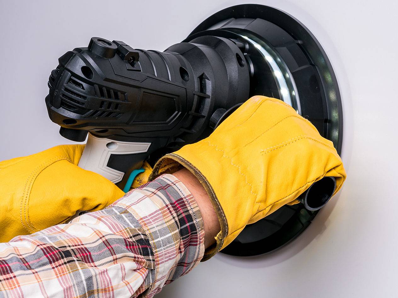Elektryczna szlifierka do ścian z oświetleniem LED, używana przez osobę w rękawicach.