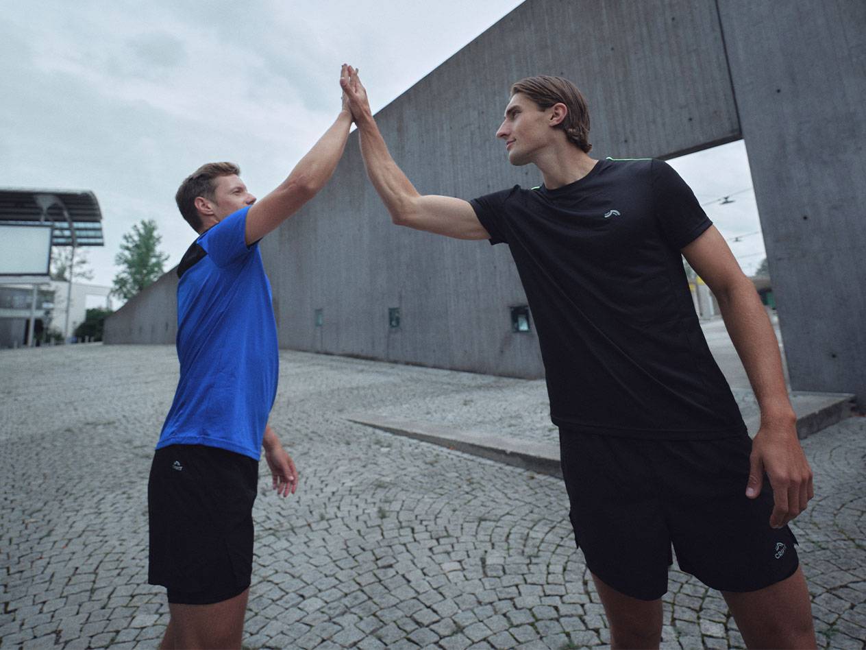 Dwóch mężczyzn w czarnych i niebieskich koszulkach sportowych i szortach przybija piątkę.