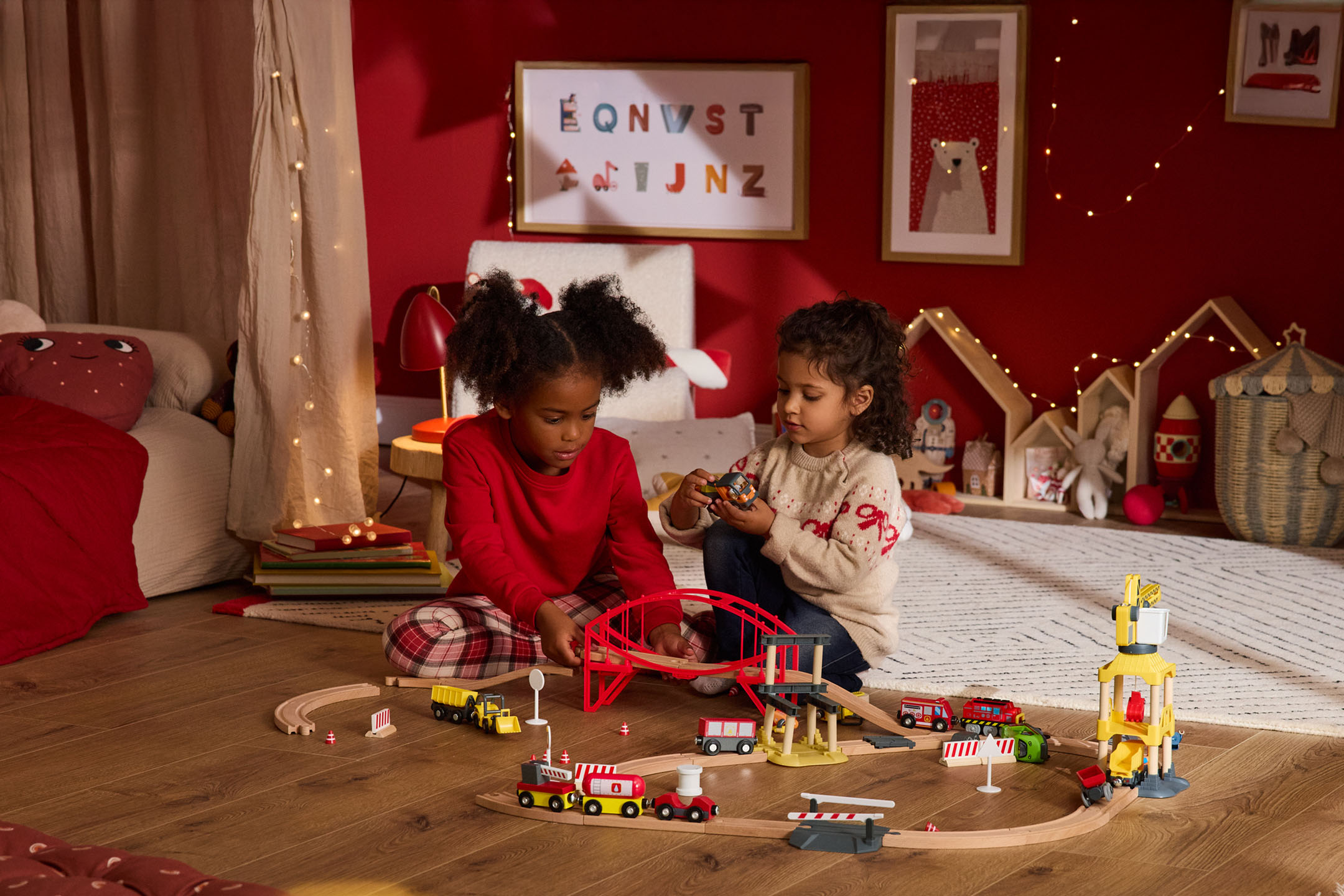 Dwoje dzieci bawi się drewnianą kolejką i zabawkami budowlanymi w pokoju o świątecznym wystroju.