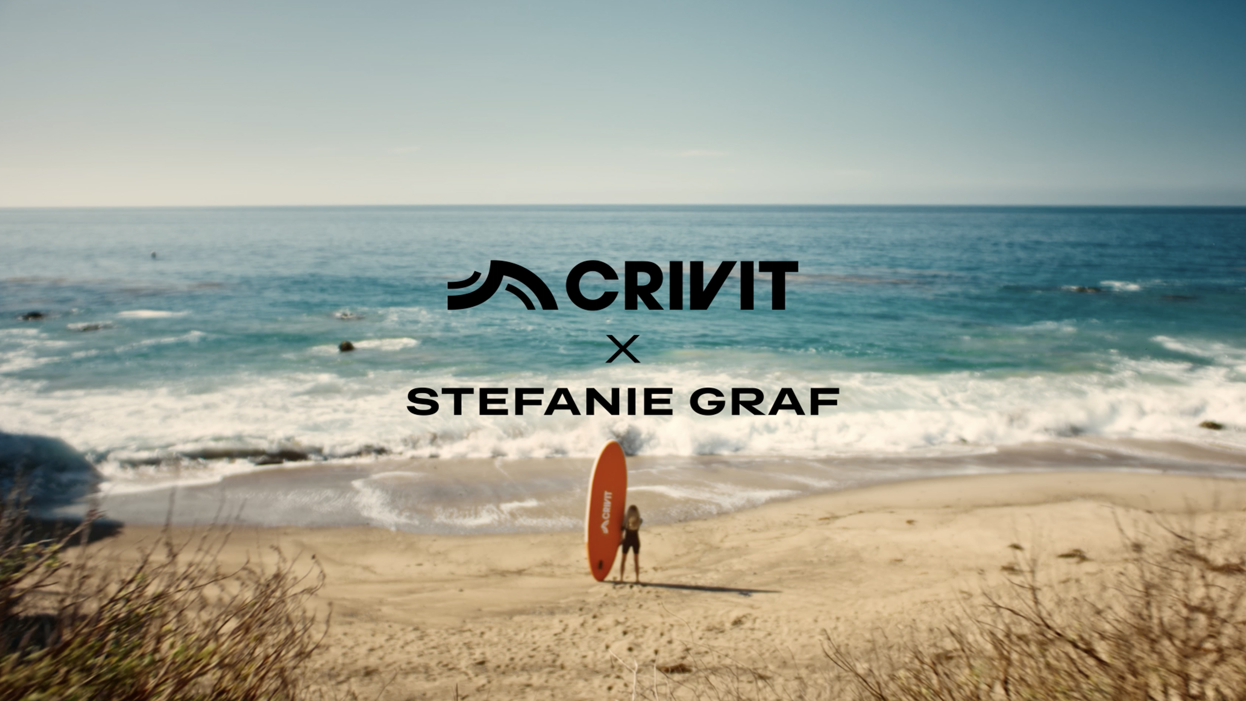 Kobieta z pomarańczową deską SUP na piaszczystej plaży, z morzem w tle.