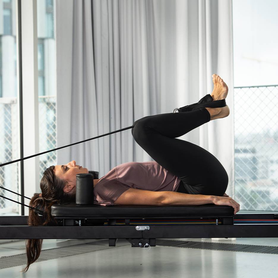Kobieta ćwiczy Pilates na reformerze z uniesionymi nogami.