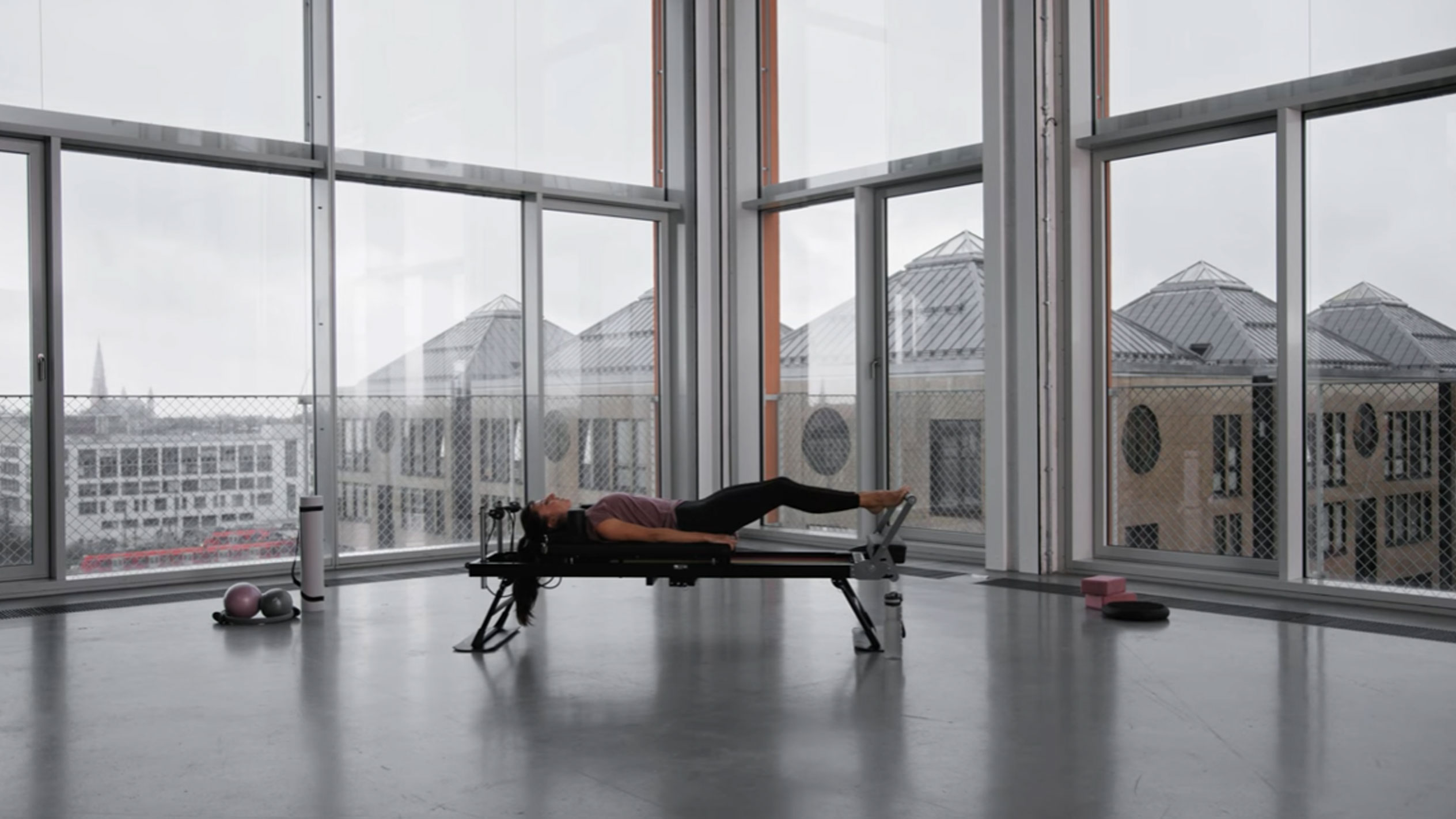 Kobieta ćwicząca Pilates w nowoczesnym studiu z widokiem na miasto.