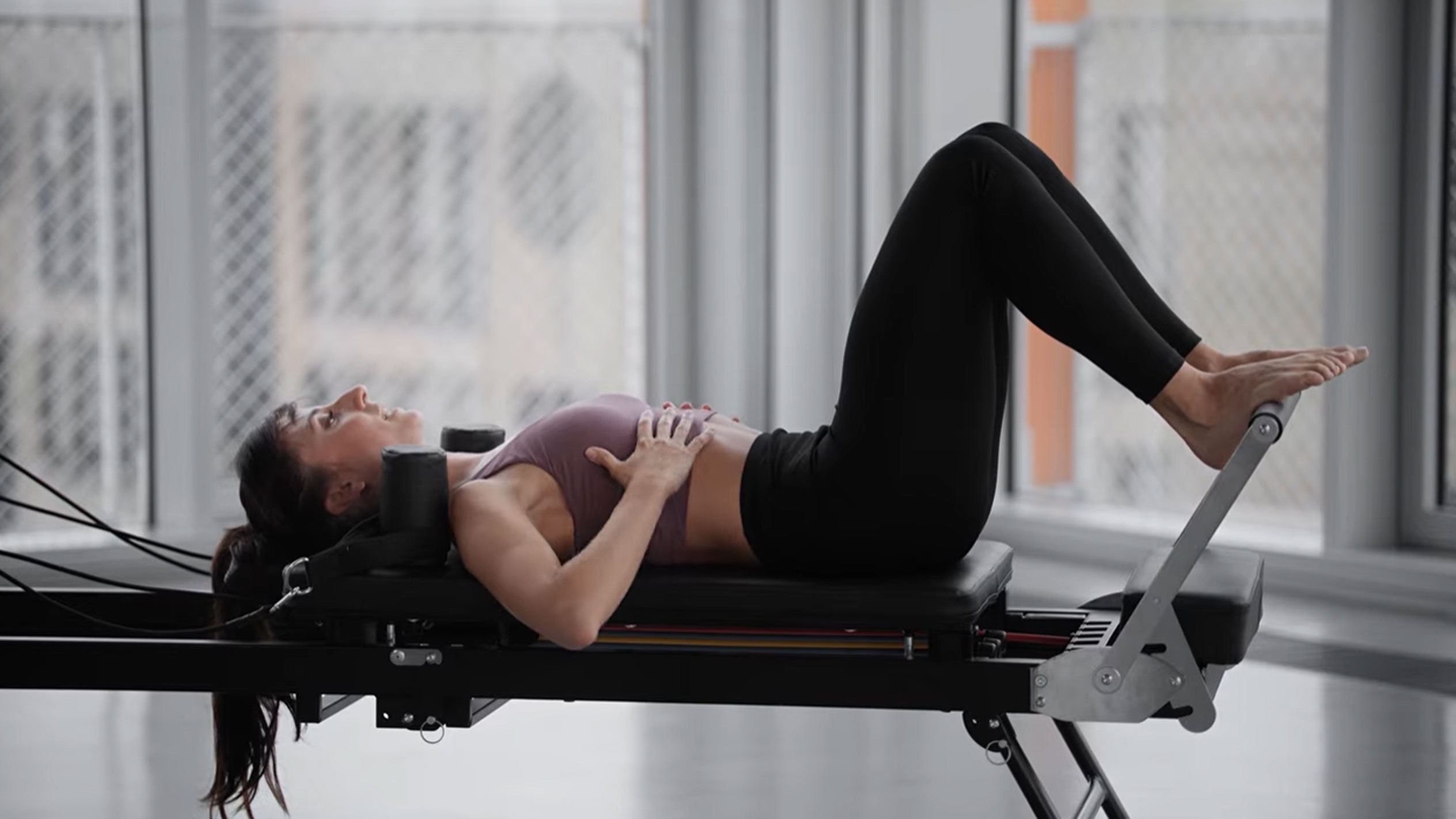 Kobieta ćwicząca Pilates na reformerze, z rękami na klatce piersiowej.