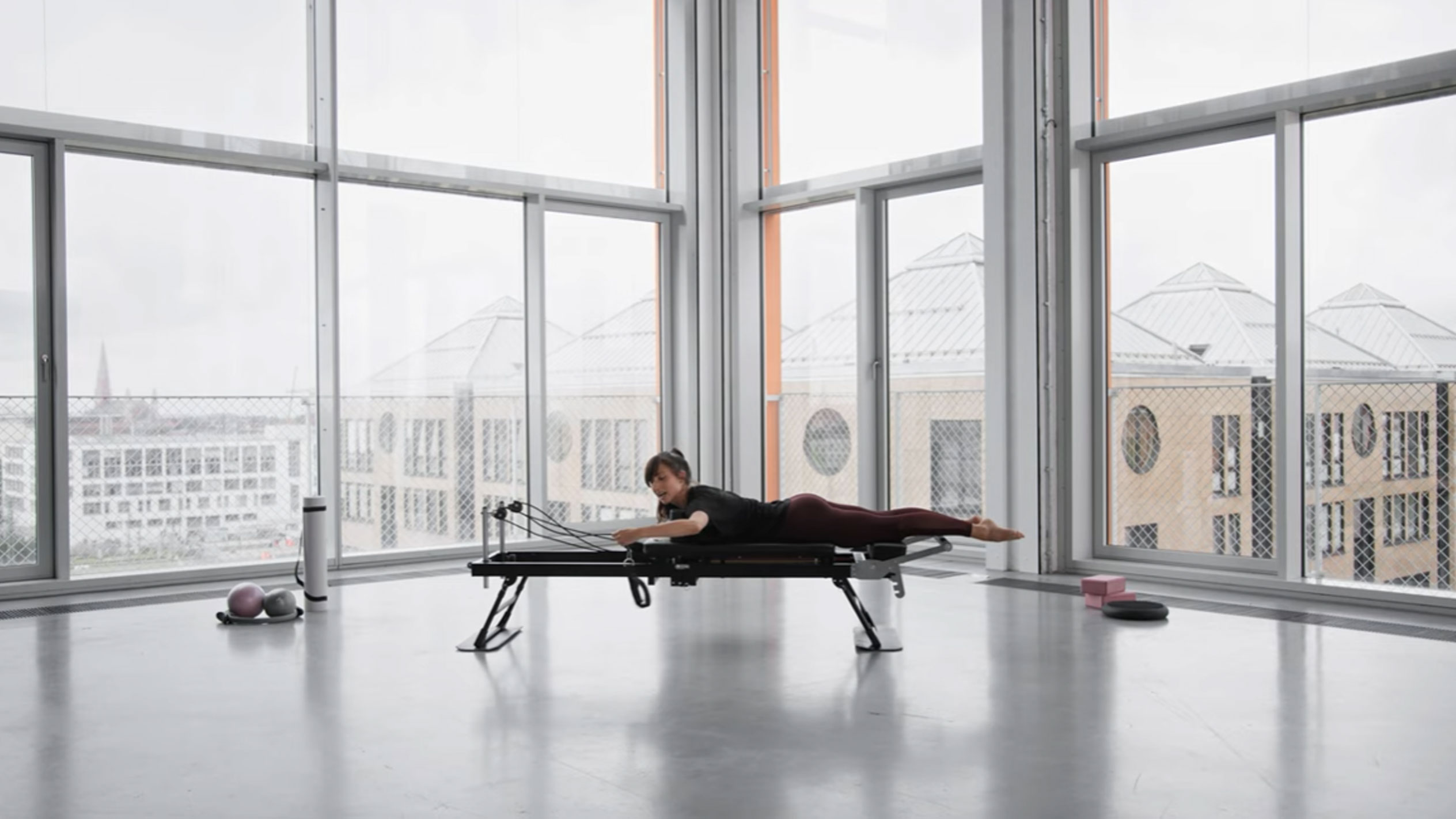 Kobieta ćwicząca Pilates na reformerze, z widokiem na miasto.