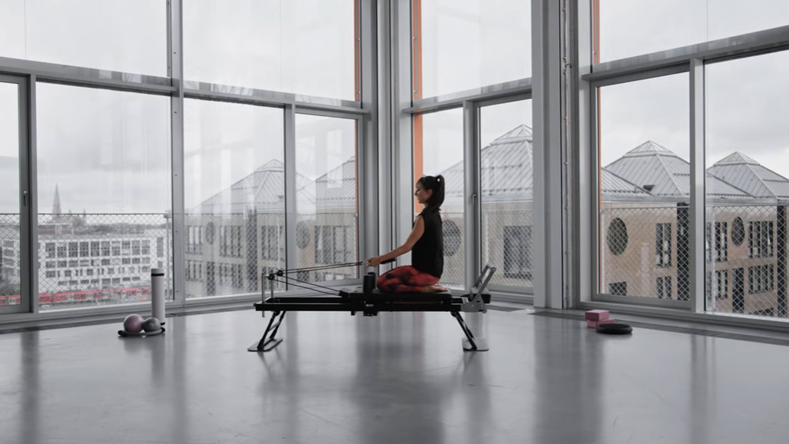 Kobieta ćwicząca Pilates na reformerze, z widokiem na miasto.