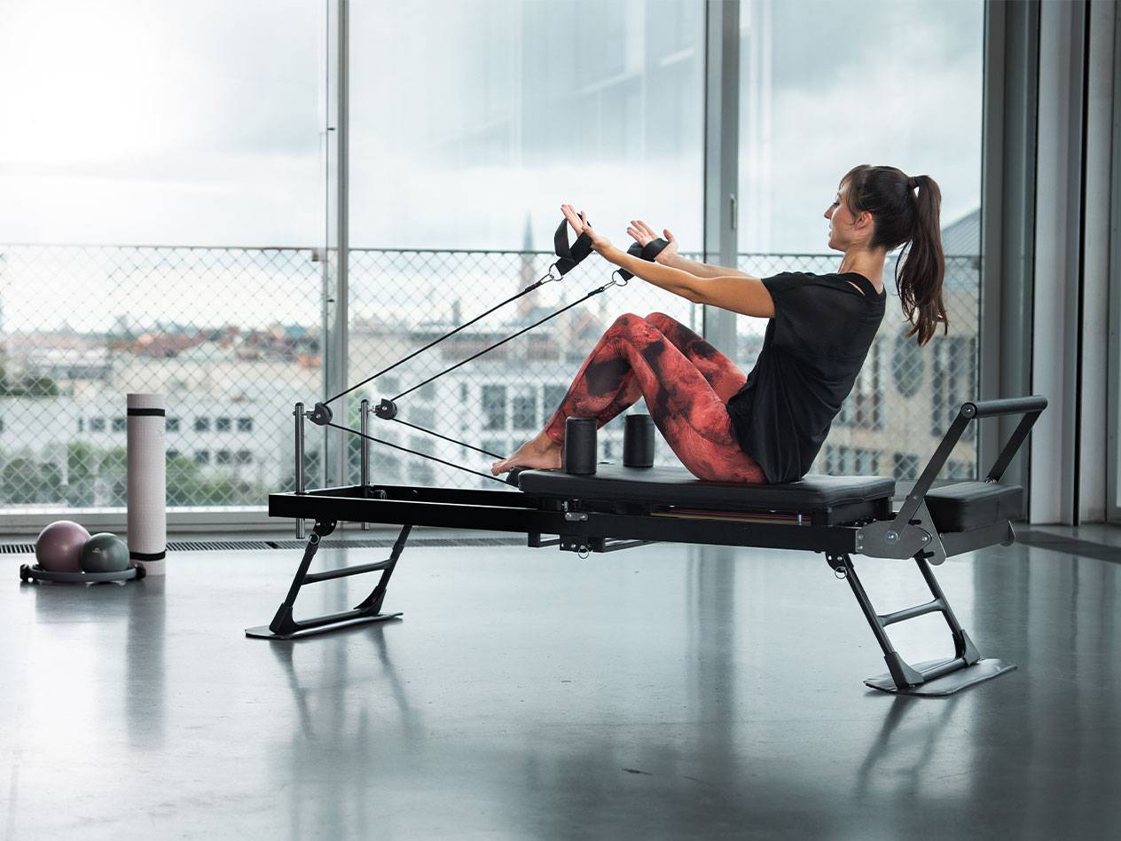 Kobieta ćwiczy pilates na reformerze z widokiem na miasto.