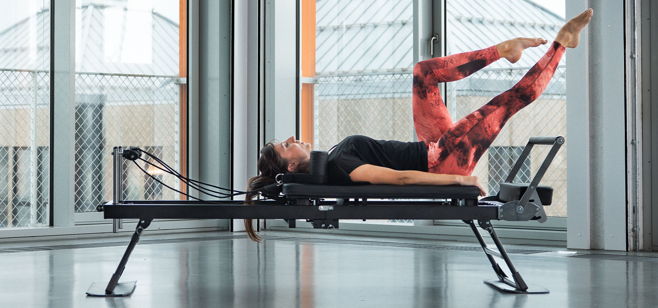 Kobieta ćwicząca Pilates na reformerze, z akcesoriami fitness w pobliżu.