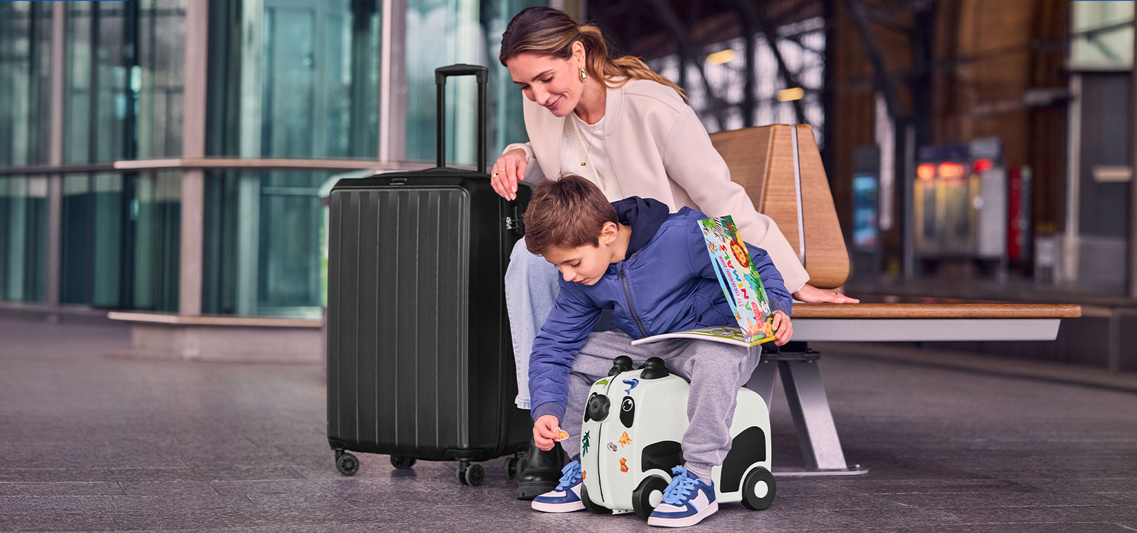 Kobieta i dziecko na lotnisku. Dziecko z walizką dziecięcą w pandy oraz mama czarną walizką na kółkach.