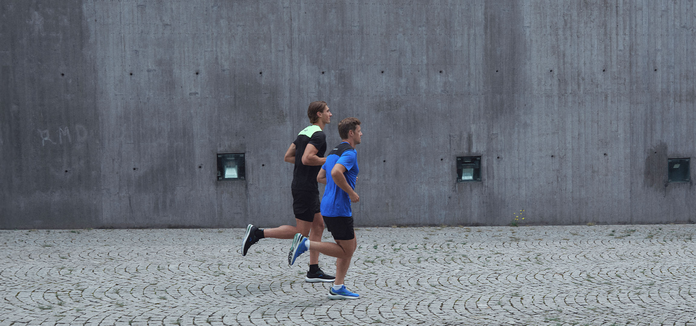 Dwóch mężczyzn w odzieży sportowej biegnie wzdłuż ściany.