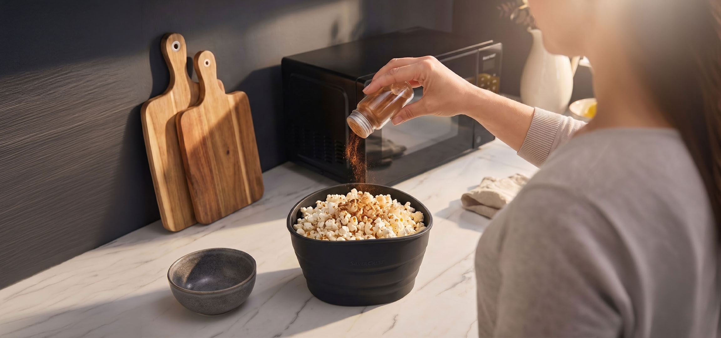Grafika została wygenerowana przy użyciu AI: Popcorn w czarnej misce przyprawiany przyprawami, obok drewnianych desek do krojenia.