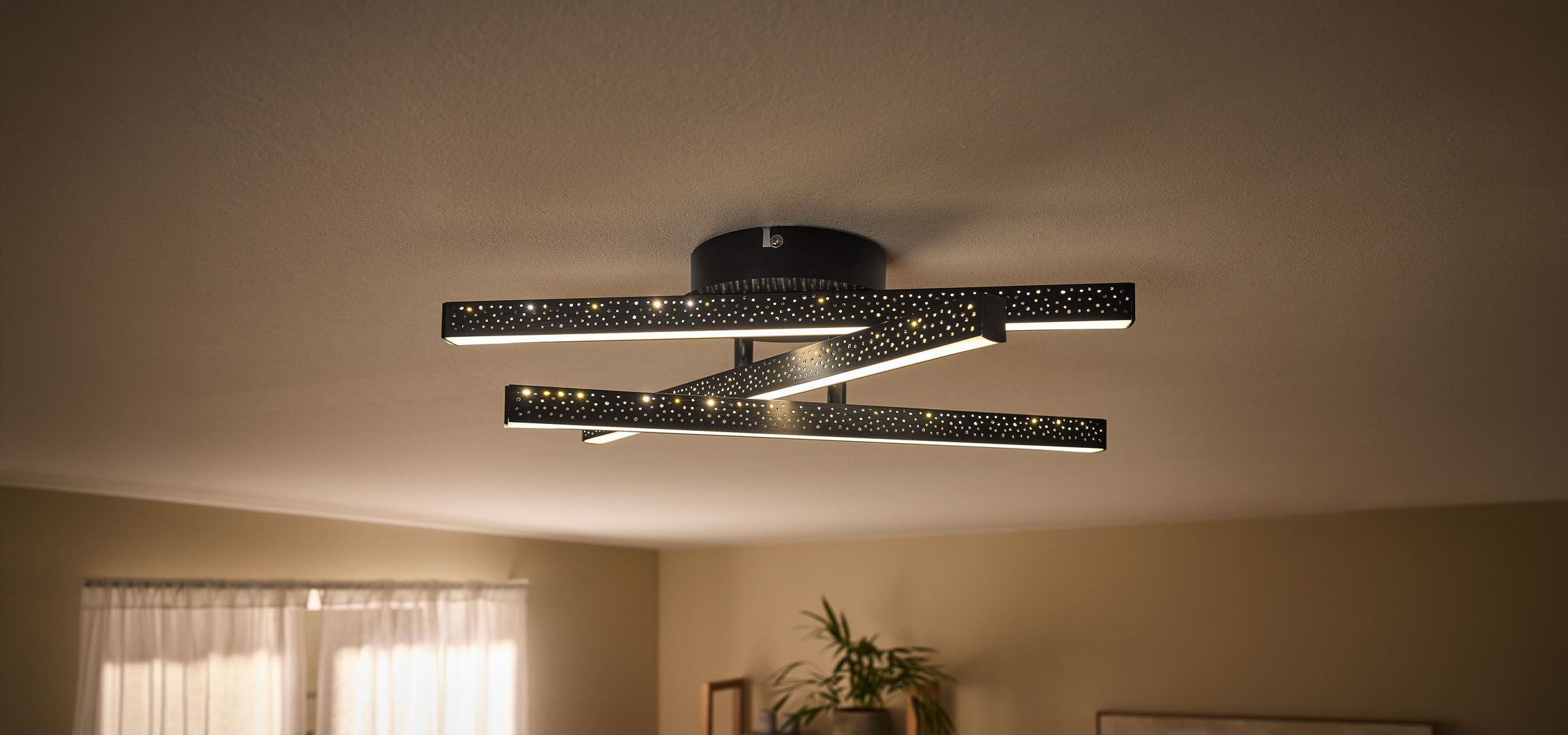 Nowoczesna lampa sufitowa LED z czarnymi, perforowanymi prętami i ciepłym światłem.