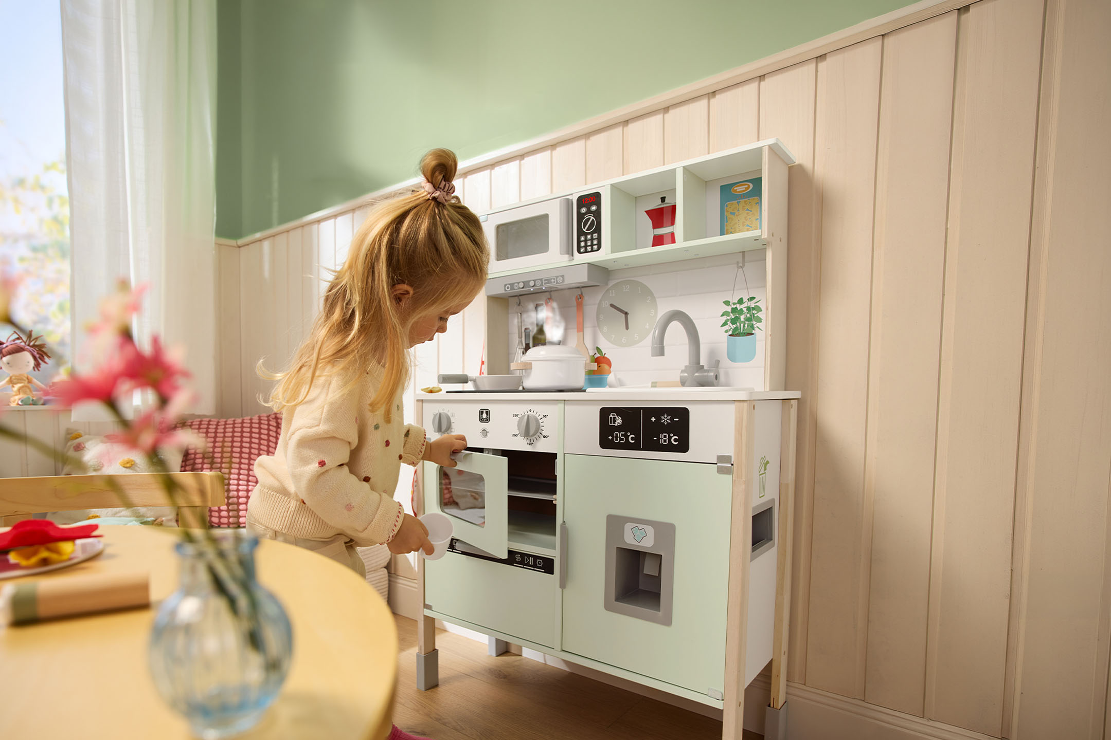 Dziewczynka bawi się drewnianą kuchnią zabawkową, otwierając drzwiczki piekarnika.