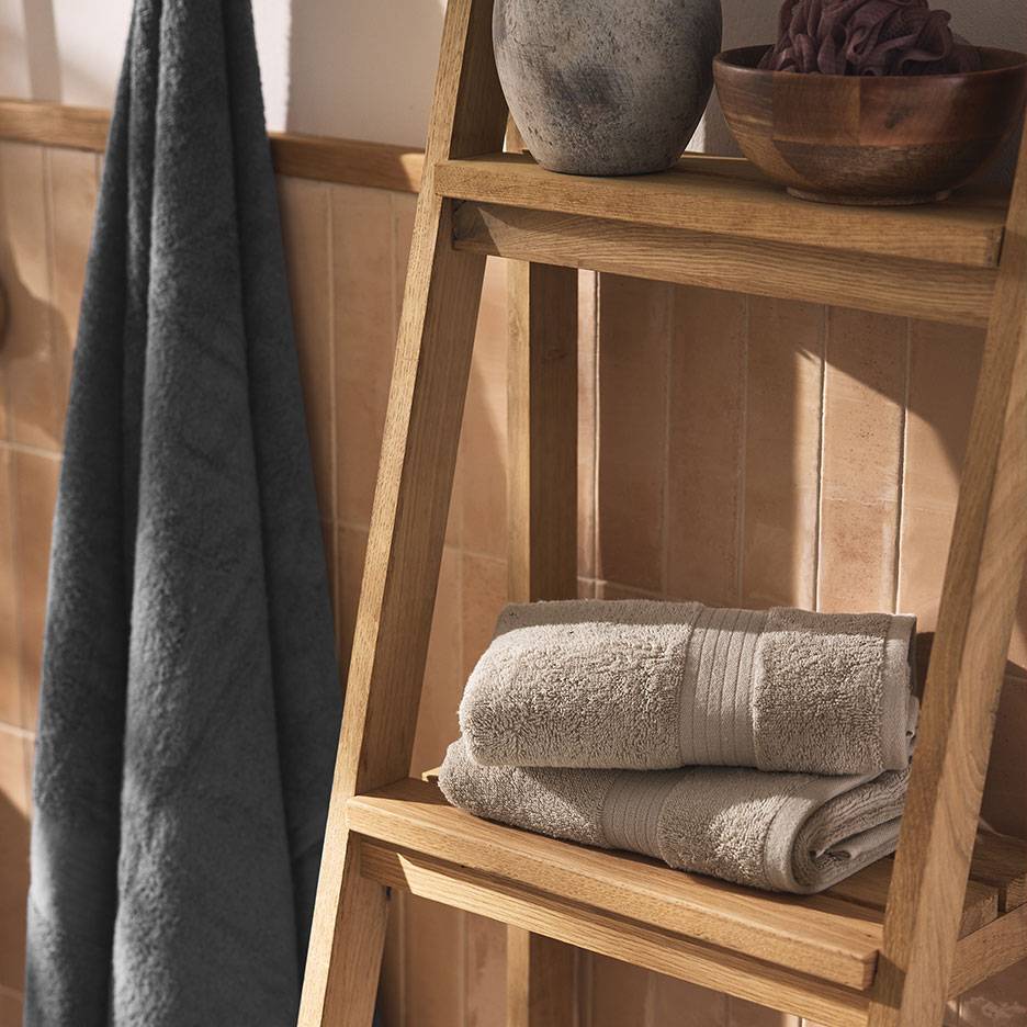 Szare ręczniki na drewnianej półce i drabinie w kafelkowej łazience.