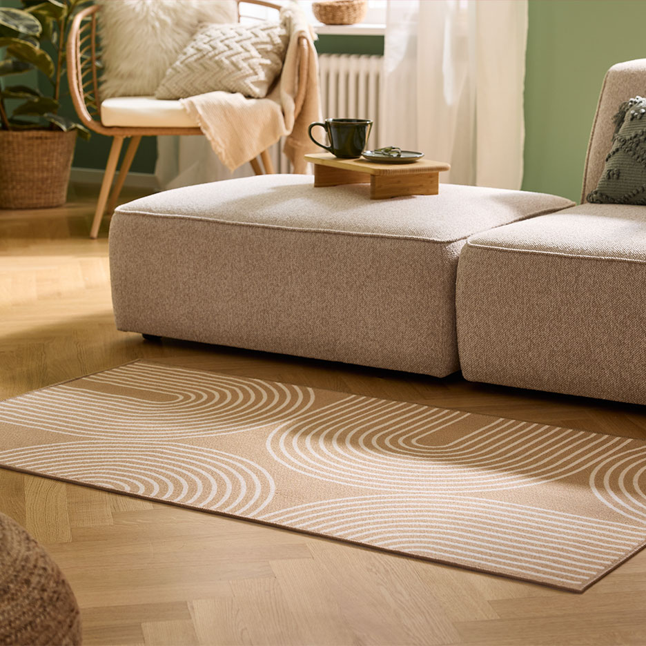 Beżowy dywan z łukowatym wzorem, modułowa sofa i drewniany fotel w przytulnym salonie.