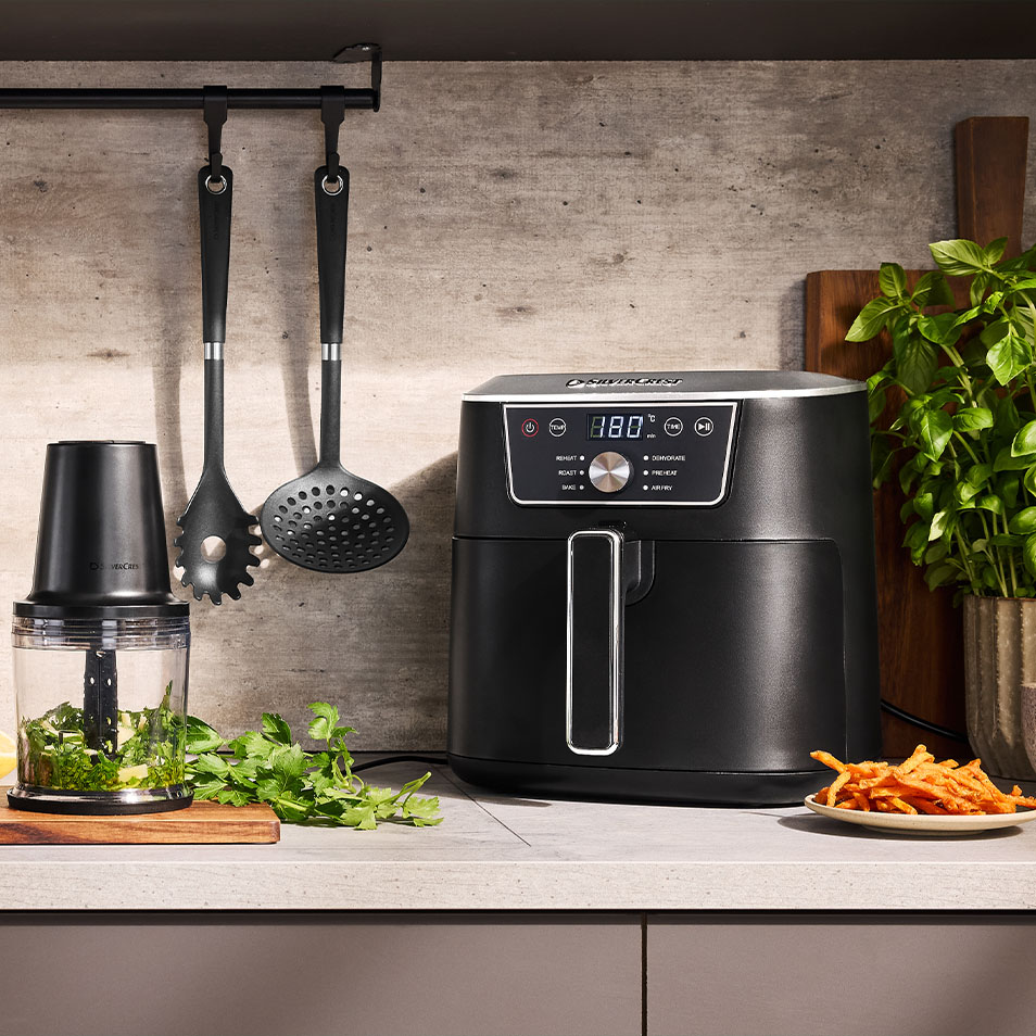 Frytkownica beztłuszczowa i rozdrabniacz SilverCrest na blacie kuchennym ze świeżymi ziołami i frytkami z batatów.