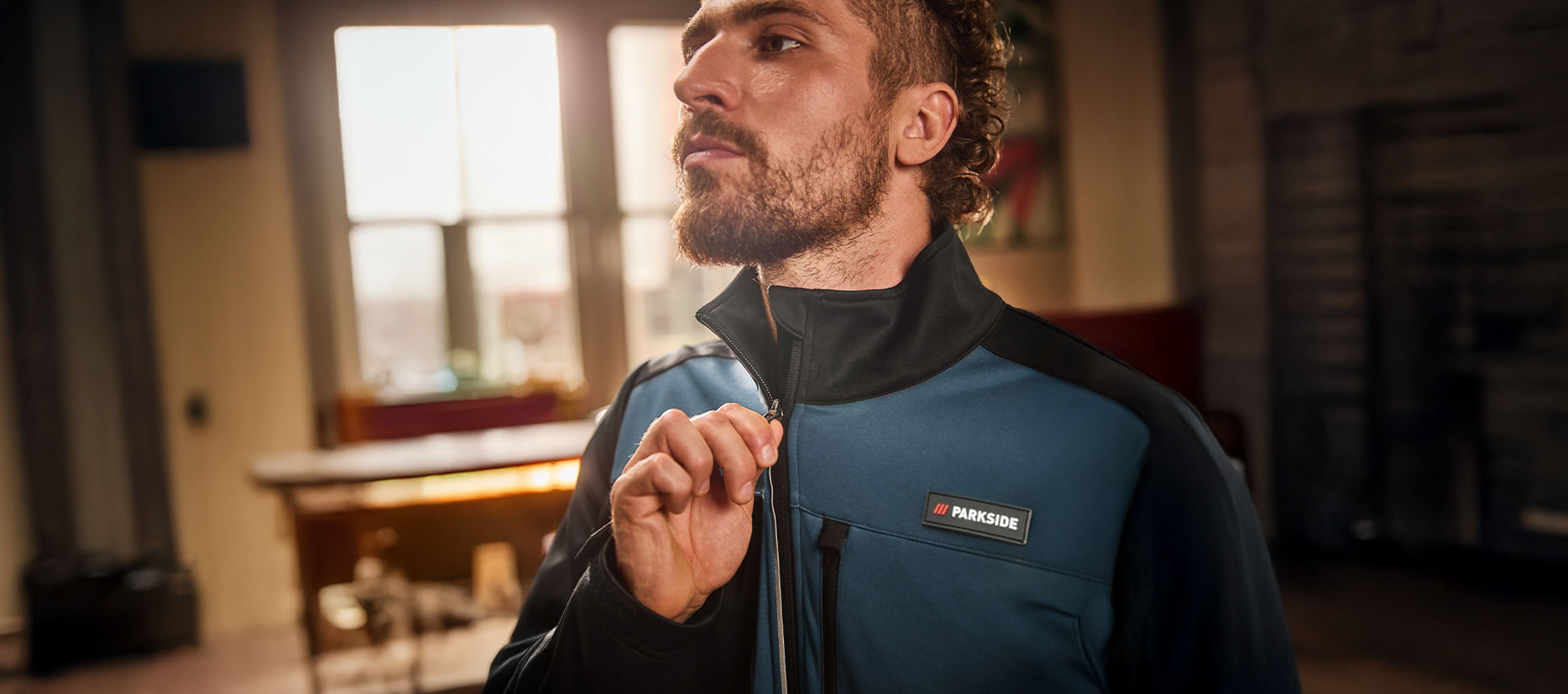 Mężczyzna w niebiesko-czarnej kurtce roboczej Parkside zapina ją