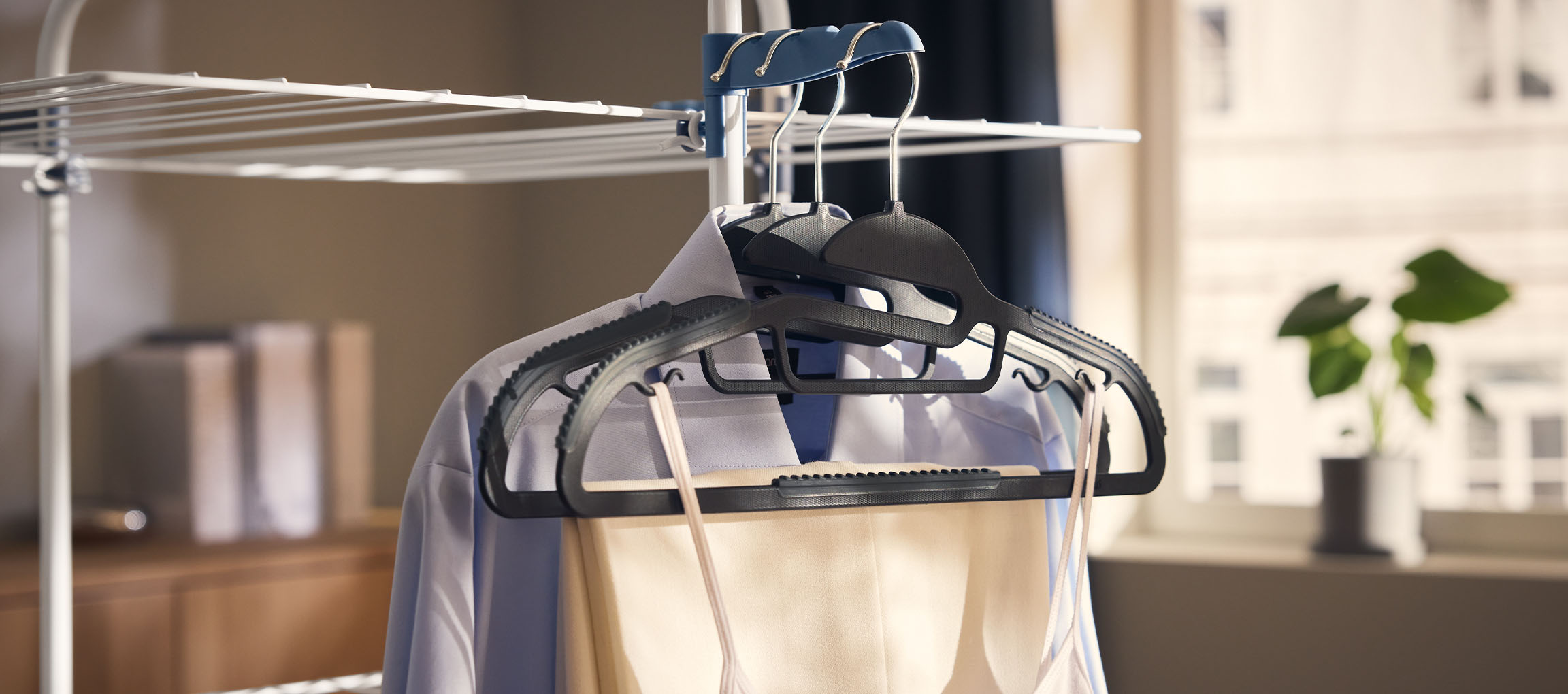 Ubrania na wieszakach na suszarce, z rośliną w tle.