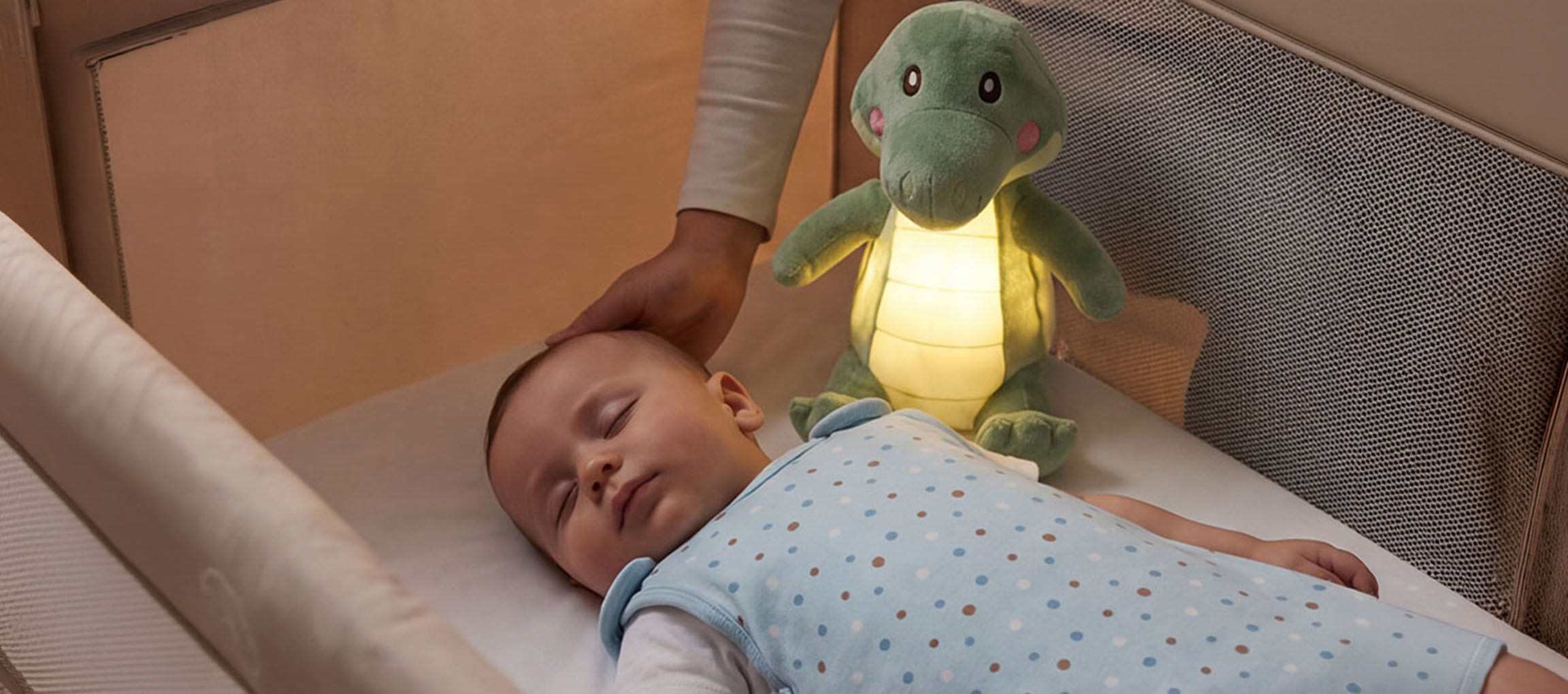 Dziecko śpi w łóżeczku z pluszową lampką nocną, dorosły głaszcze dziecko po głowie.
