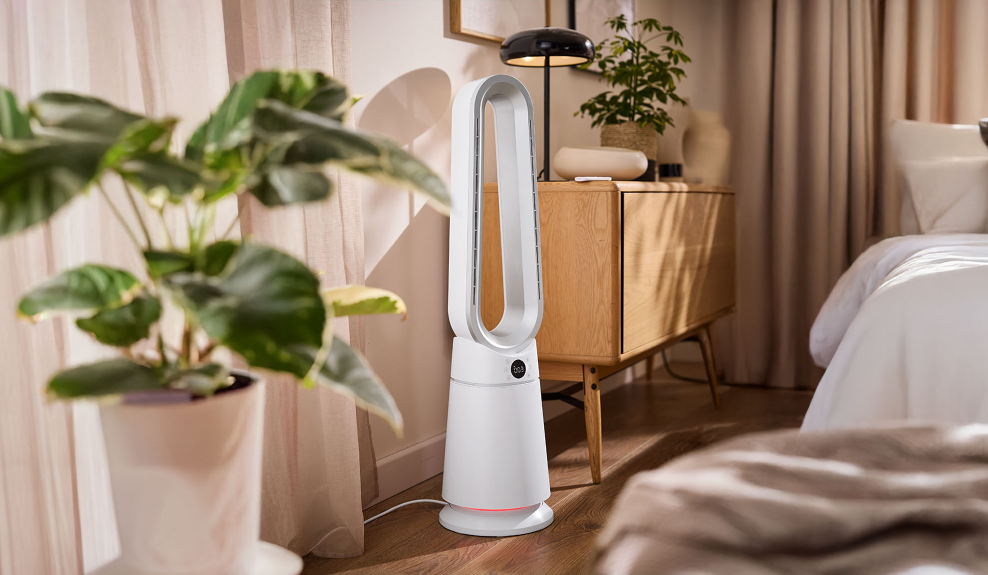 Biały wentylator kolumnowy w nowoczesnej sypialni z roślinami i drewnianymi meblami.