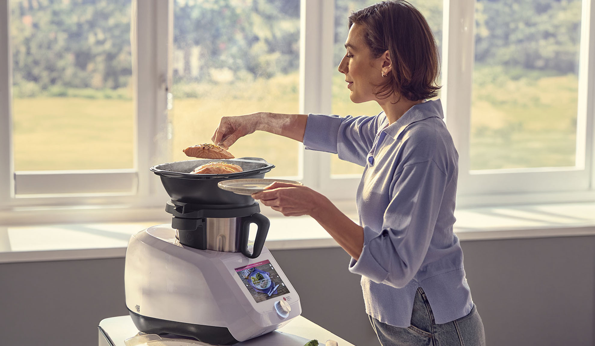 Kobieta gotuje łososia w robocie kuchennym z funkcją gotowania na parze, korzystając z cyfrowego ekranu.