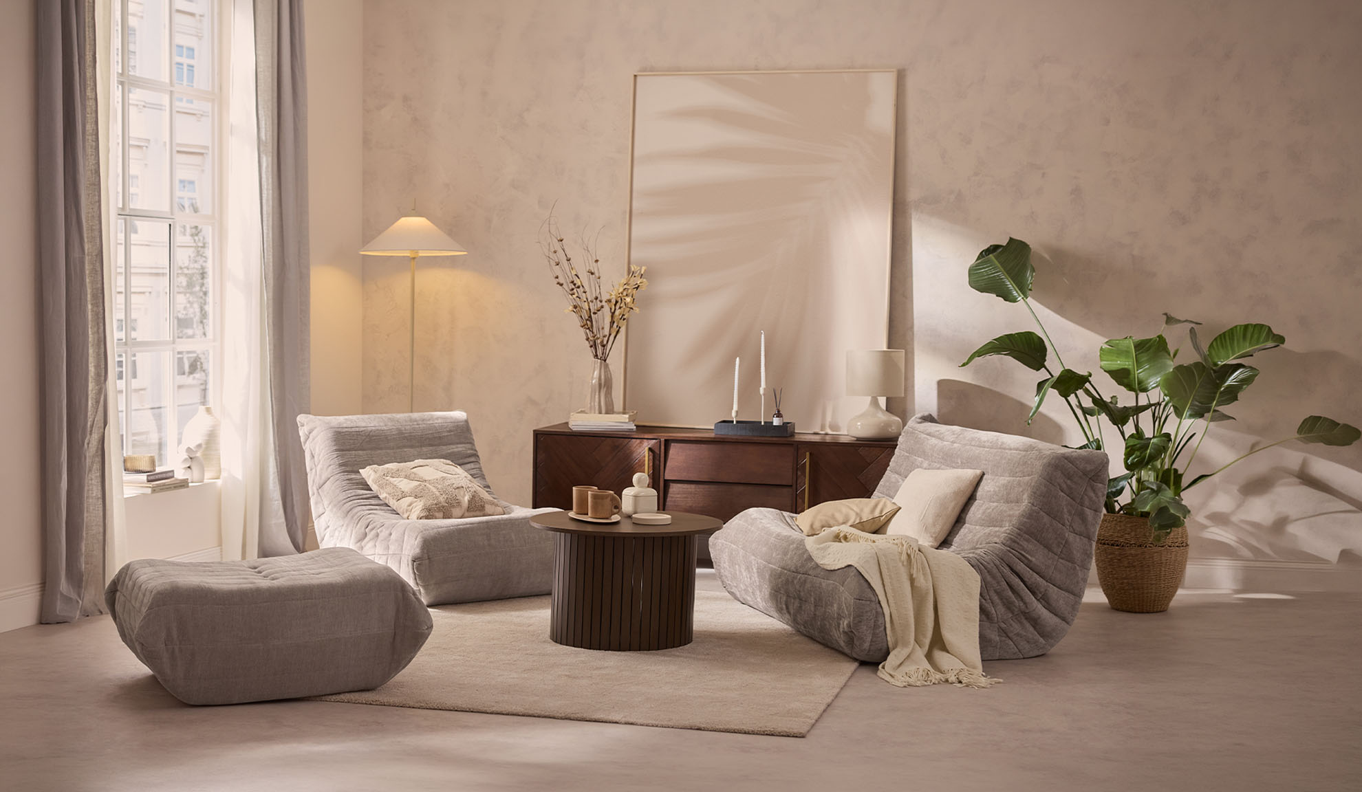 Przytulny salon z dwoma szarymi fotelami wypoczynkowymi, pufą, stolikiem kawowym i rośliną.