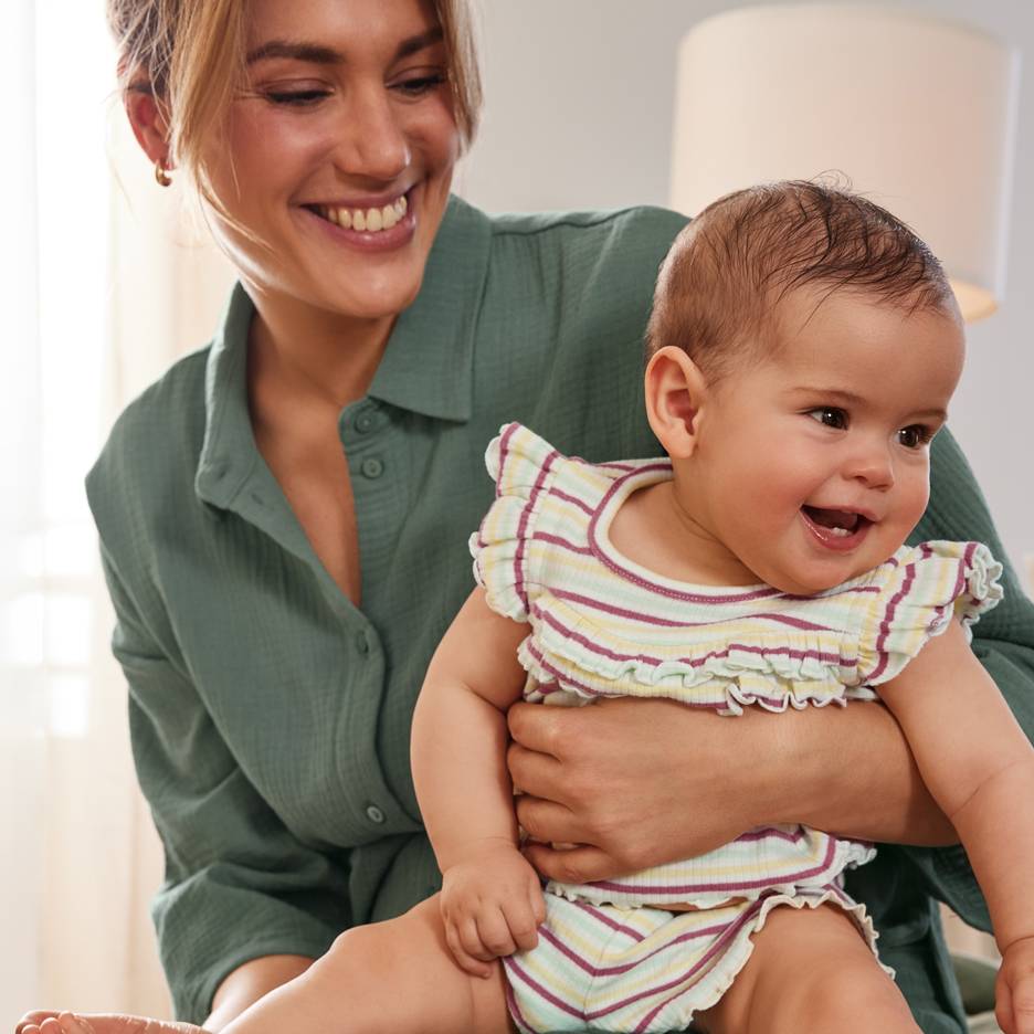 Uśmiechnięta mama z radosnym niemowlakiem, ubranym w kolorowy strój w paski.