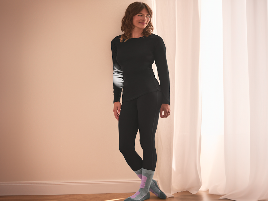 Kobieta w czarnej bieliźnie termicznej i skarpetkach, oparta o ścianę.